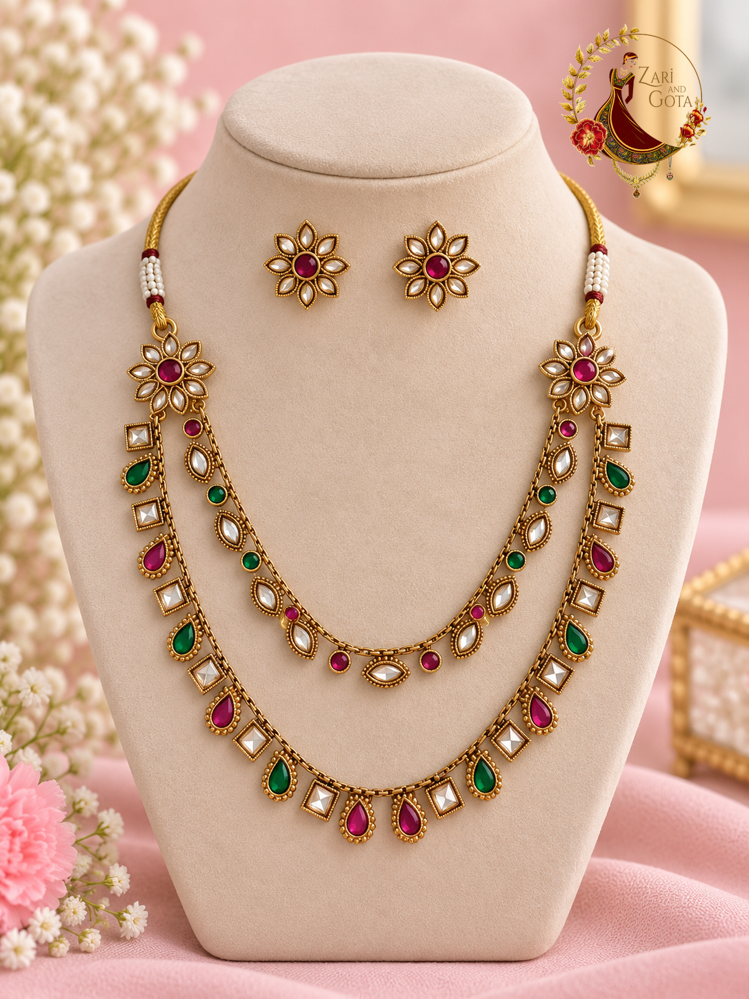 Ruby, emerald and white kundan gold-finish two-strand necklace set with flower stud earrings on a display bust, Zari and Gota UK