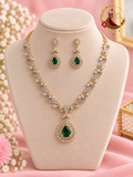 Gold-tone American diamond wave necklace with emerald green pear pendant and matching earrings on a display bust, Zari and Gota UK