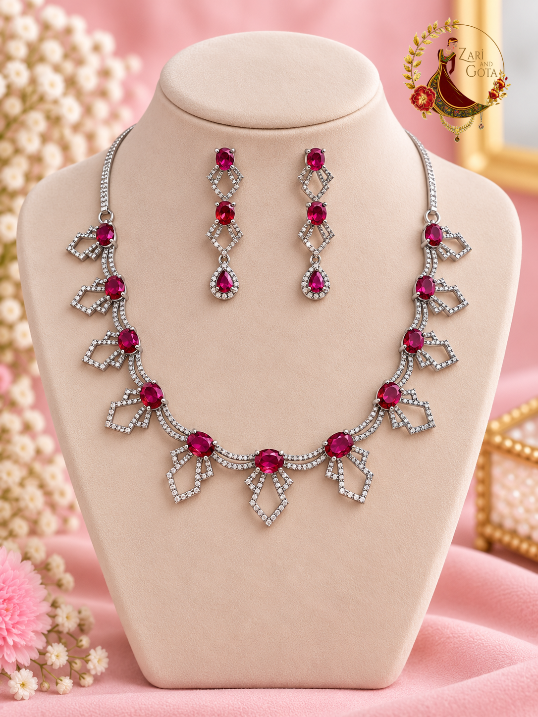 Silver-tone geometric American diamond necklace with ruby red ovals and matching drop earrings on a display bust, Zari and Gota UK