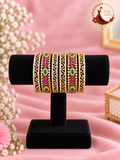 Set of six gold-tone bangles with ruby-pink and emerald green stones and American diamond filigree on a black velvet stand, Zari and Gota UK