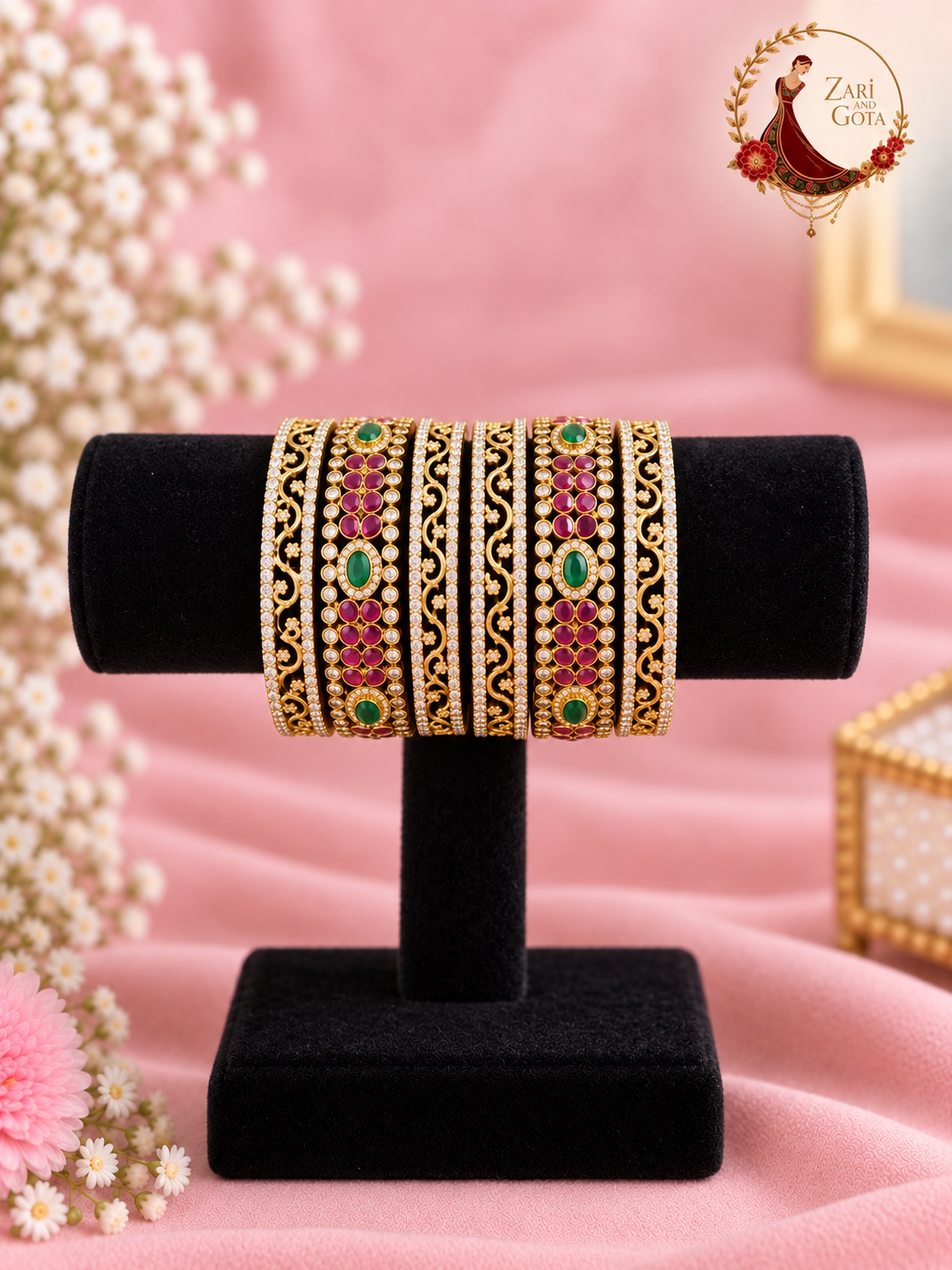 Set of six gold-tone bangles with ruby-pink and emerald green stones and American diamond filigree on a black velvet stand, Zari and Gota UK