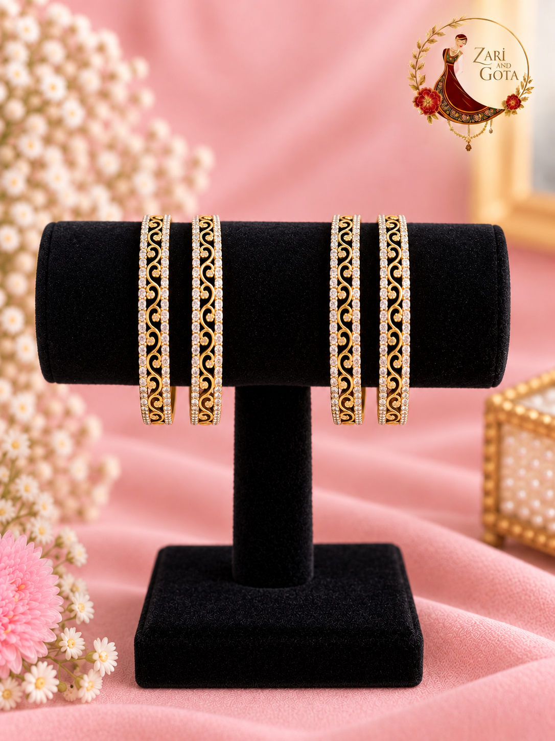 Set of four slim gold-tone openwork scroll filigree bangles edged with American diamonds on a black velvet stand, Zari and Gota UK