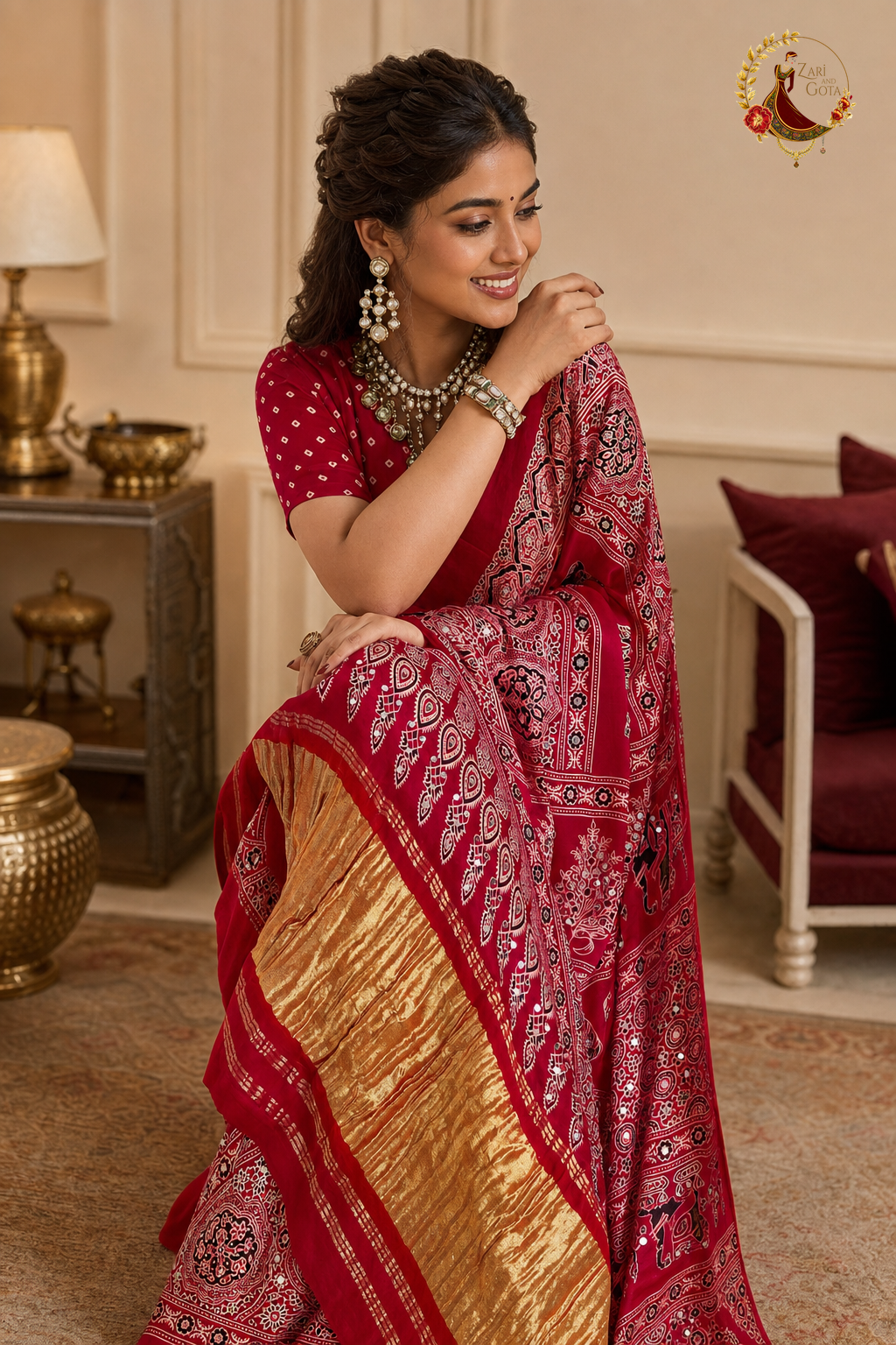 Seated view of red Gaji silk saree showing gold tissue border and mirror work detail