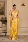 Golden yellow tissue cotton saree with pink embroidered buds and gold zari border, worn by a model