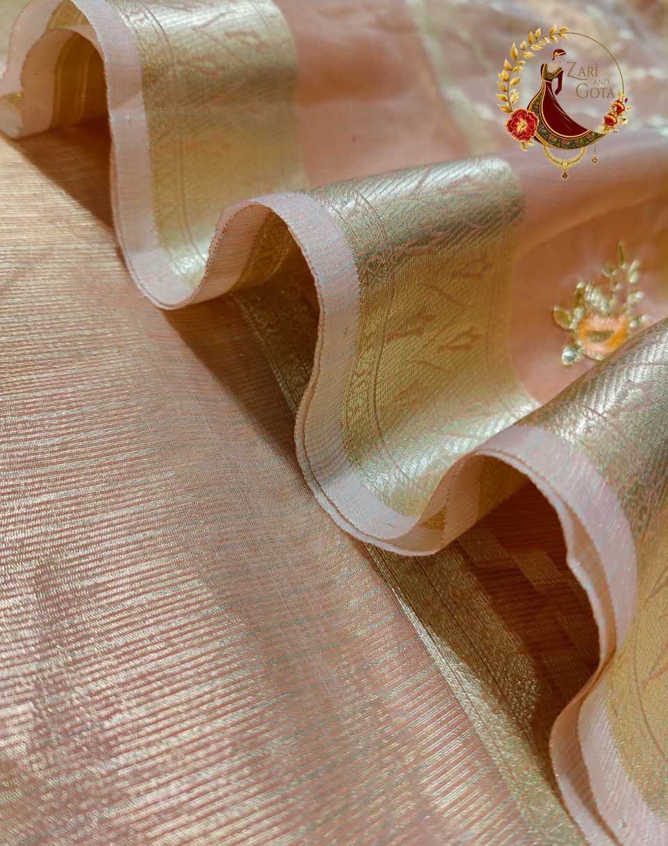 Folded peach tissue saree showing the broad gold zari pallu bands